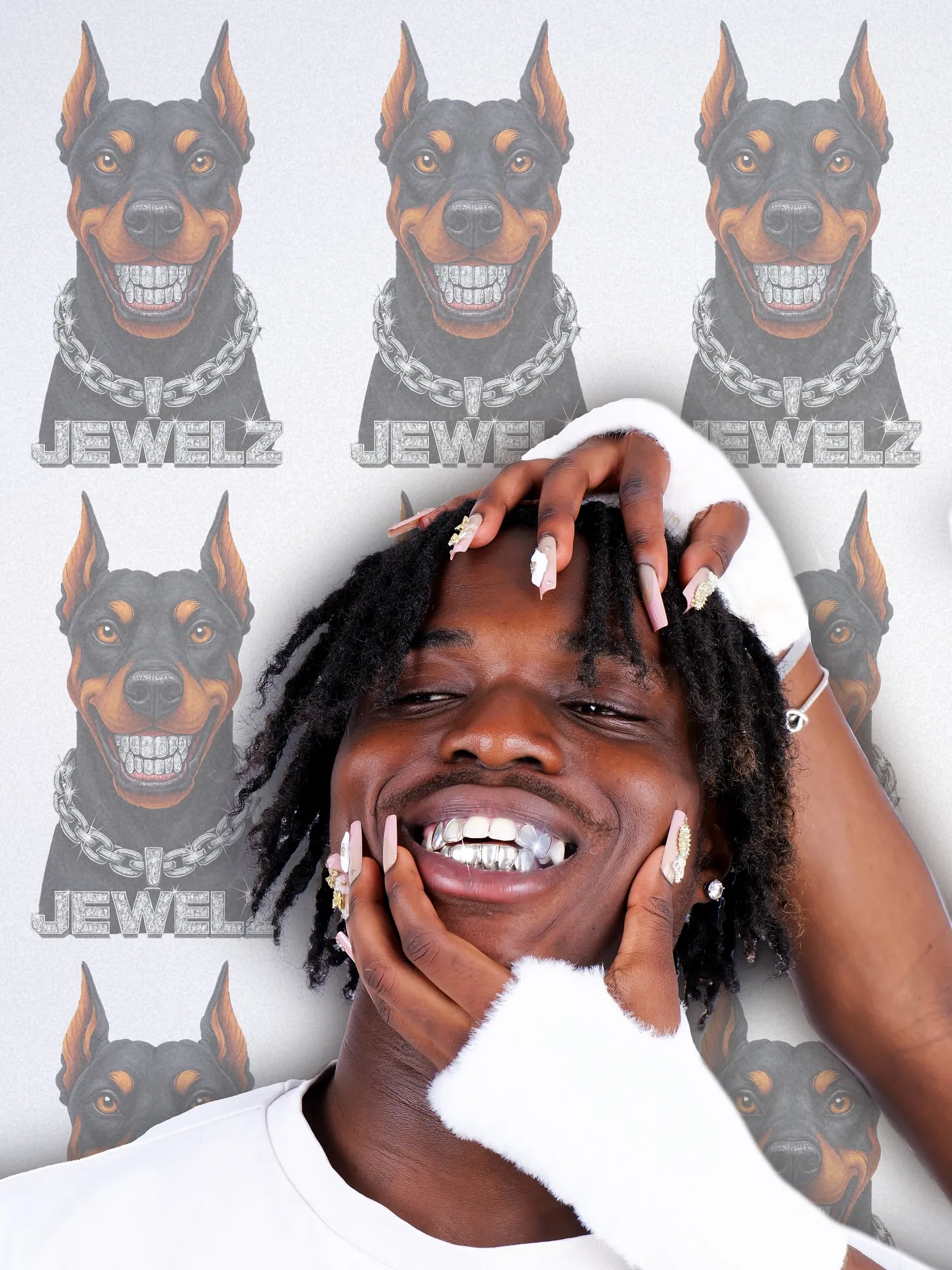 A smiling man with a silver grill, hands on his face, in front of a repeating Doberman JEWELZ logo wallpaper