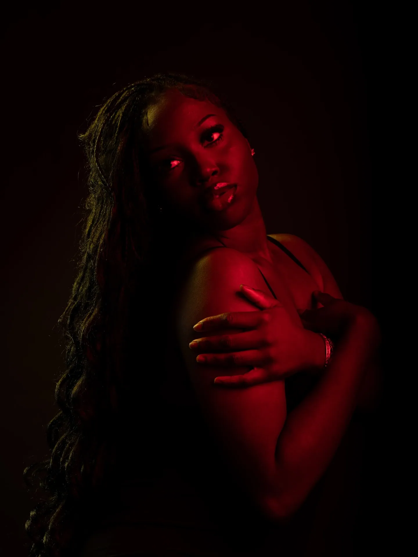 Woman looking back over her shoulder with a hand across her chest, red-lit skin against black