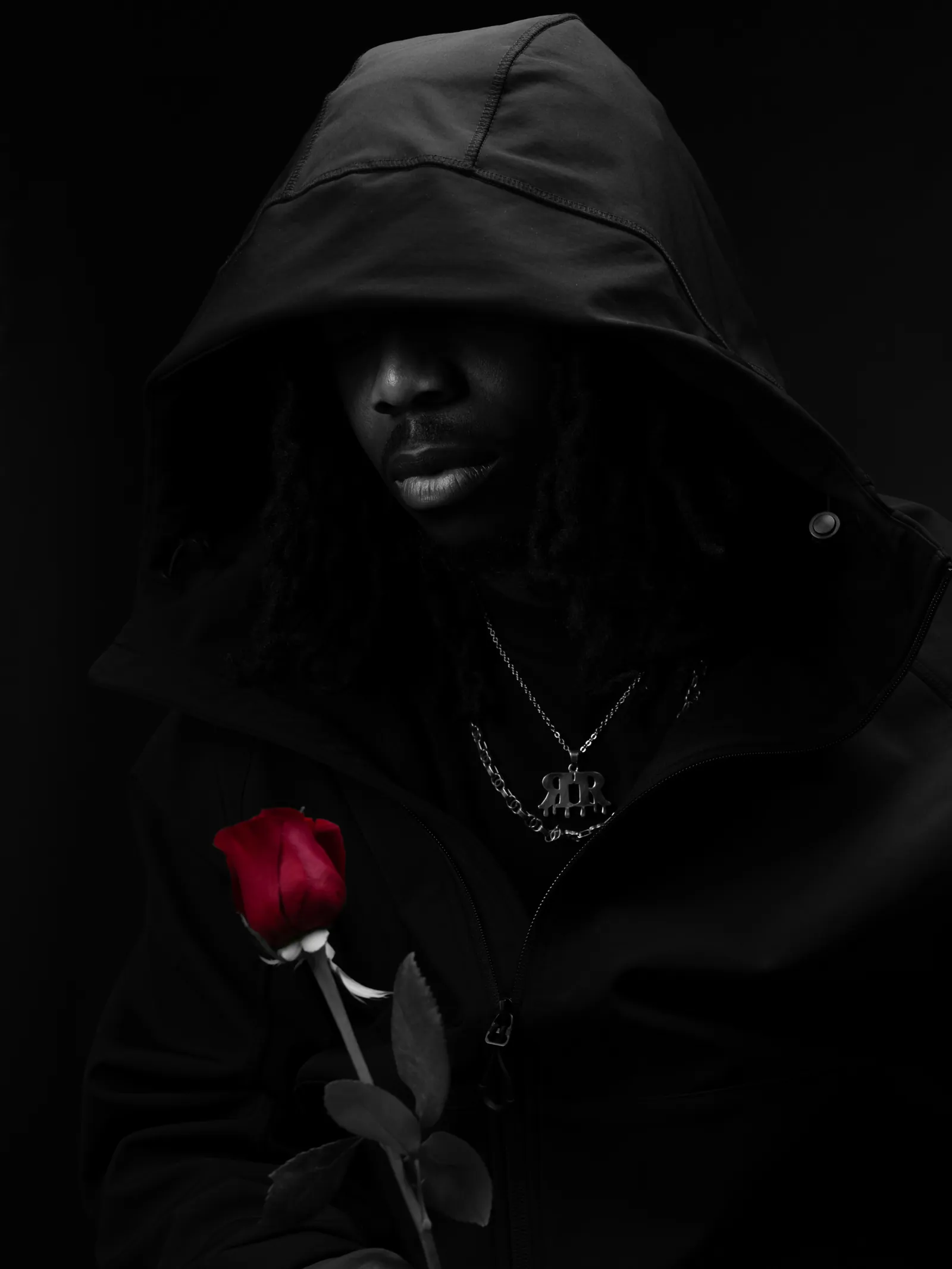 Black and white portrait of a man in a hood with a chain, holding a single red rose that is the only colour