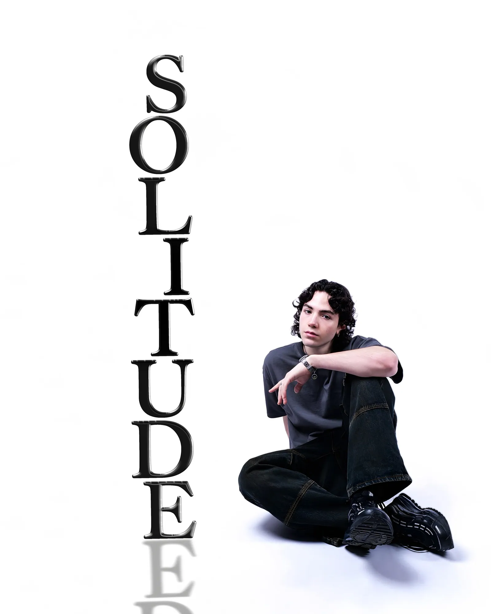 A young man sitting on the floor in a grey tee and black trousers beside the word SOLITUDE stacked vertically, white backdrop