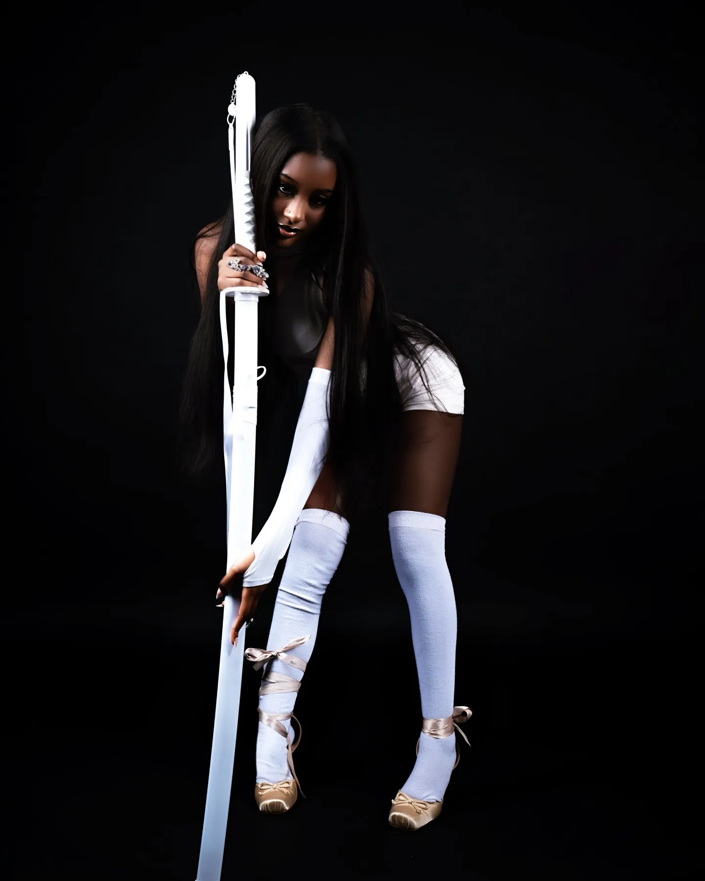 A woman in white leaning forward over a katana, long hair falling forward, thigh-high socks and gold heels, black backdrop