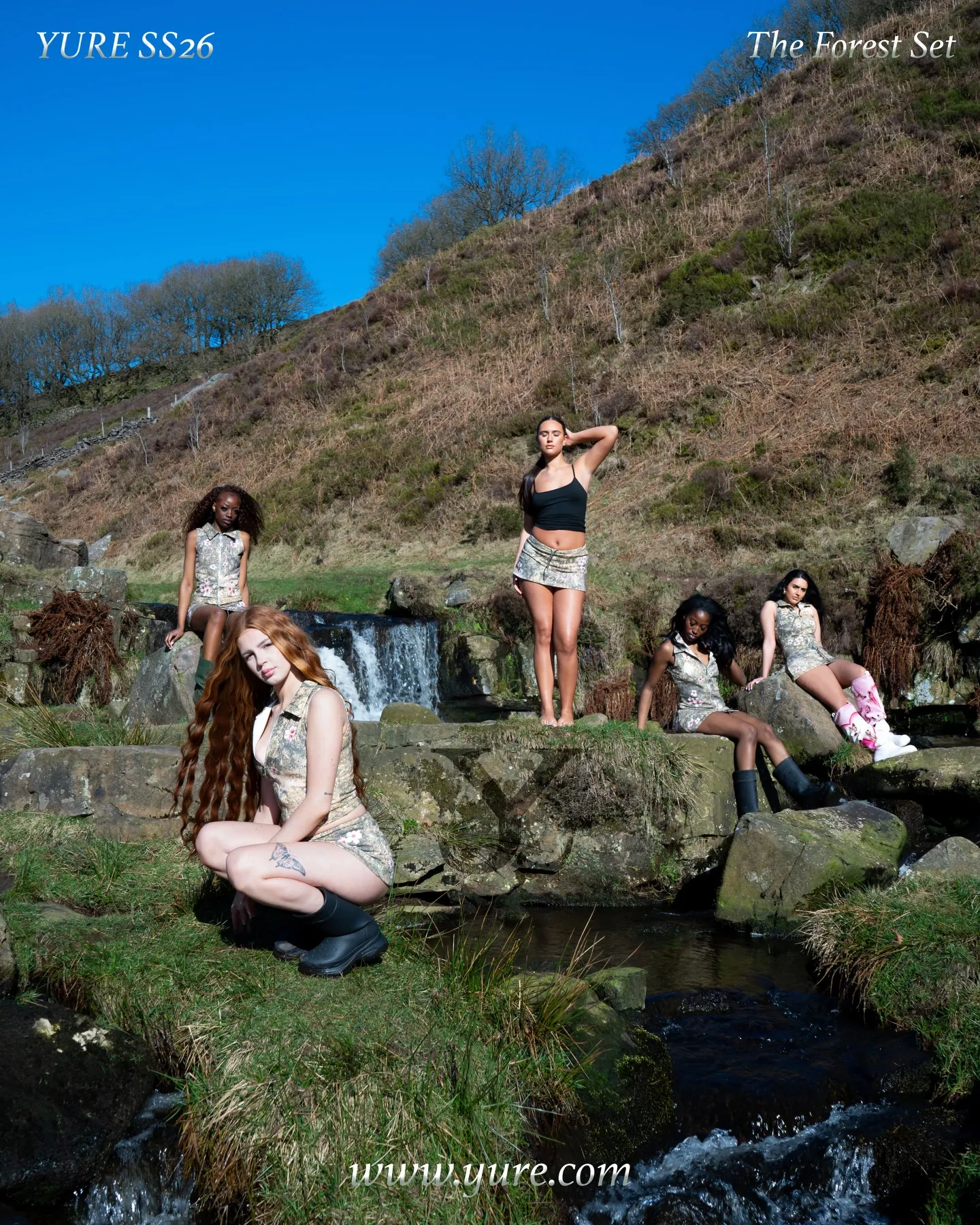 Campaign poster reading YURE SS26 The Forest Set, with five models in camo outfits around a stream and hillside