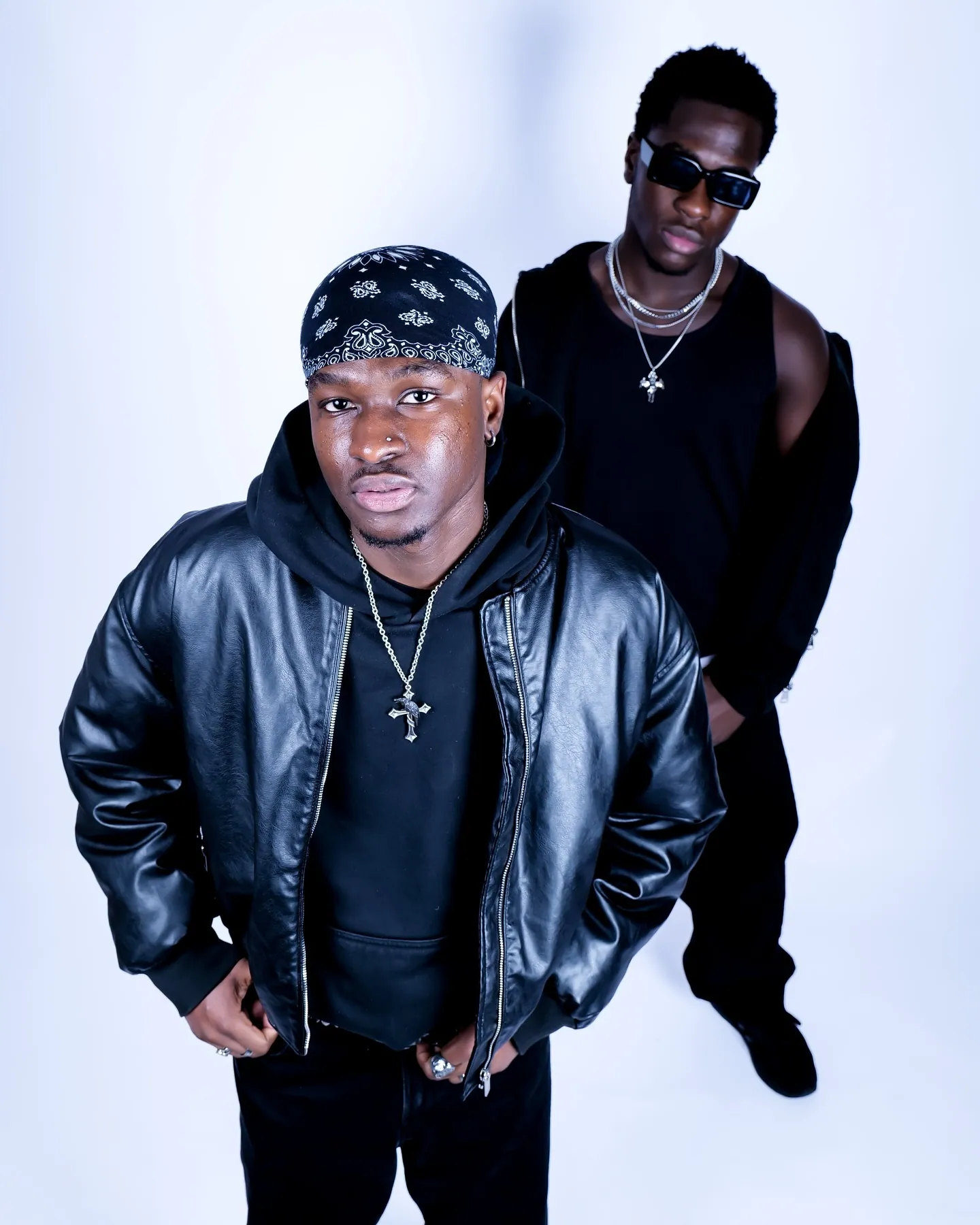 Two men seen from above, one in a bandana and black leather jacket, the other behind in sunglasses and a black vest